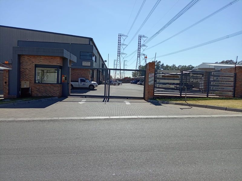 Front entrance view of a business park featuring a secure gated access point, brick guardhouse, and paved driveway.