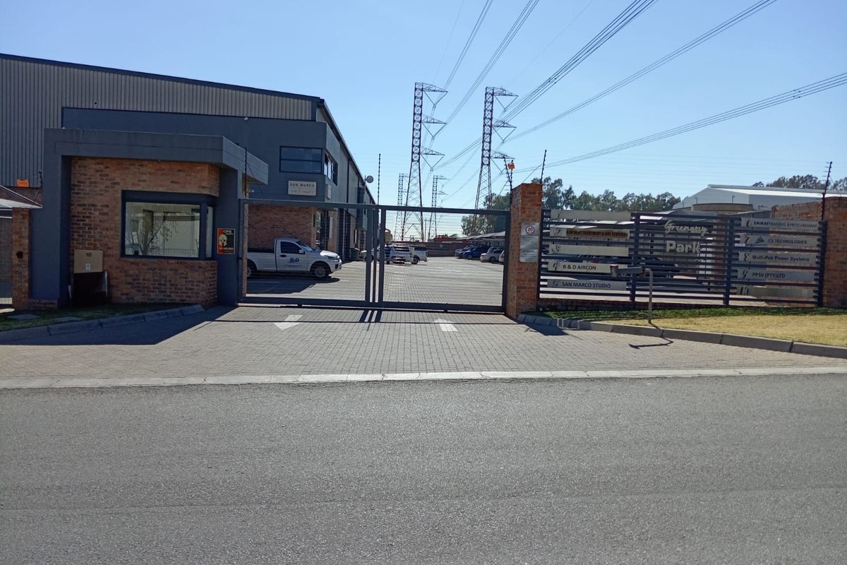 Front entrance view of a business park featuring a secure gated access point, brick guardhouse, and paved driveway.