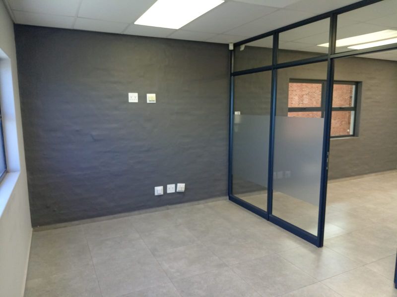 A modern, empty office space featuring grey textured walls, tiled flooring, and a glass partition wall with frosted detailing.