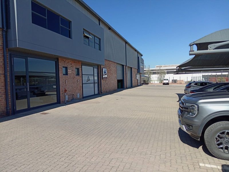 Exterior view of a modern industrial business park featuring paved parking, exposed brick facade, and secure roller shutter access points.