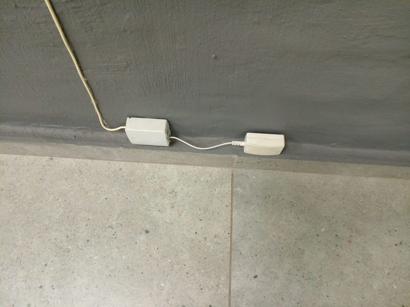 A close-up view of surface-mounted electrical wiring and a junction box installed on a painted wall above tiled flooring.