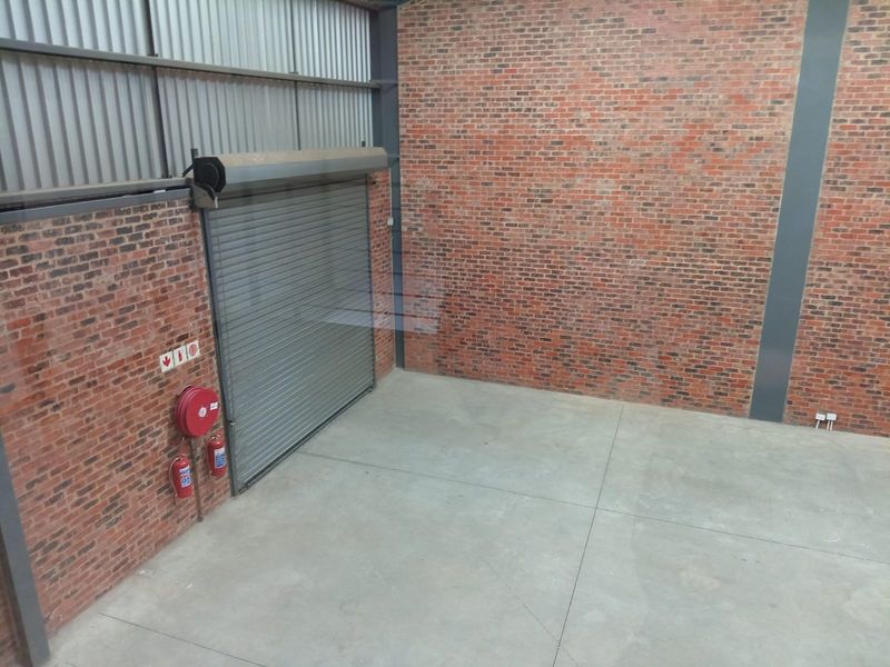 An empty industrial utility space featuring exposed brick walls, concrete flooring, and a large roller shutter door with integrated fire safety equipment.