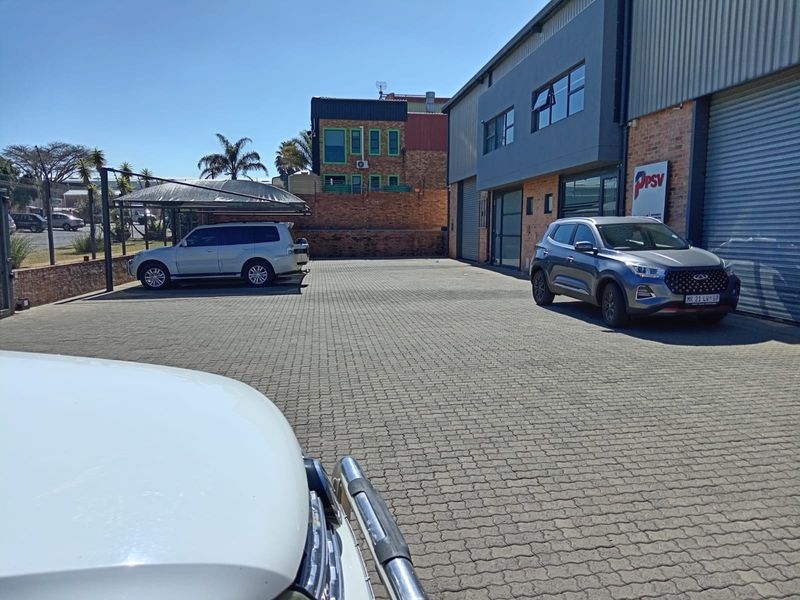 Exterior view of a commercial property featuring a paved parking area, shade cloth carport, and industrial roller shutter access.