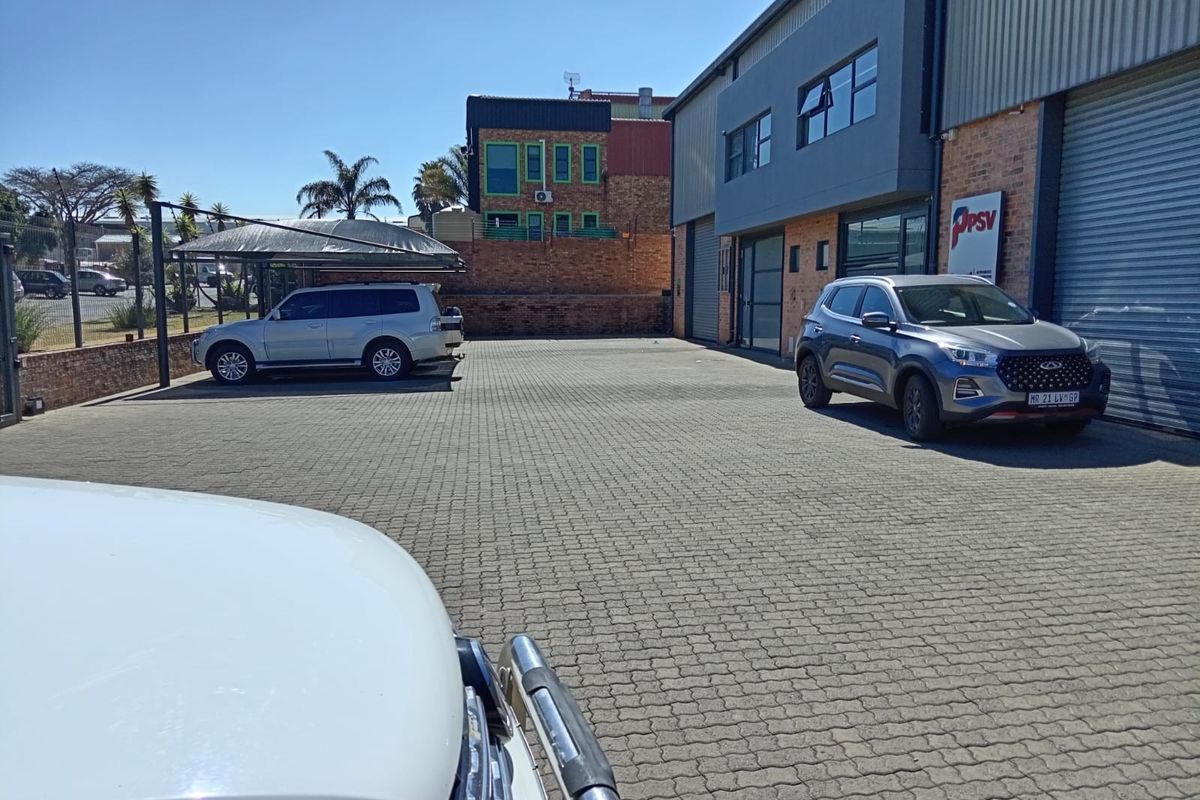 Exterior view of a commercial property featuring a paved parking area, shade cloth carport, and industrial roller shutter access.