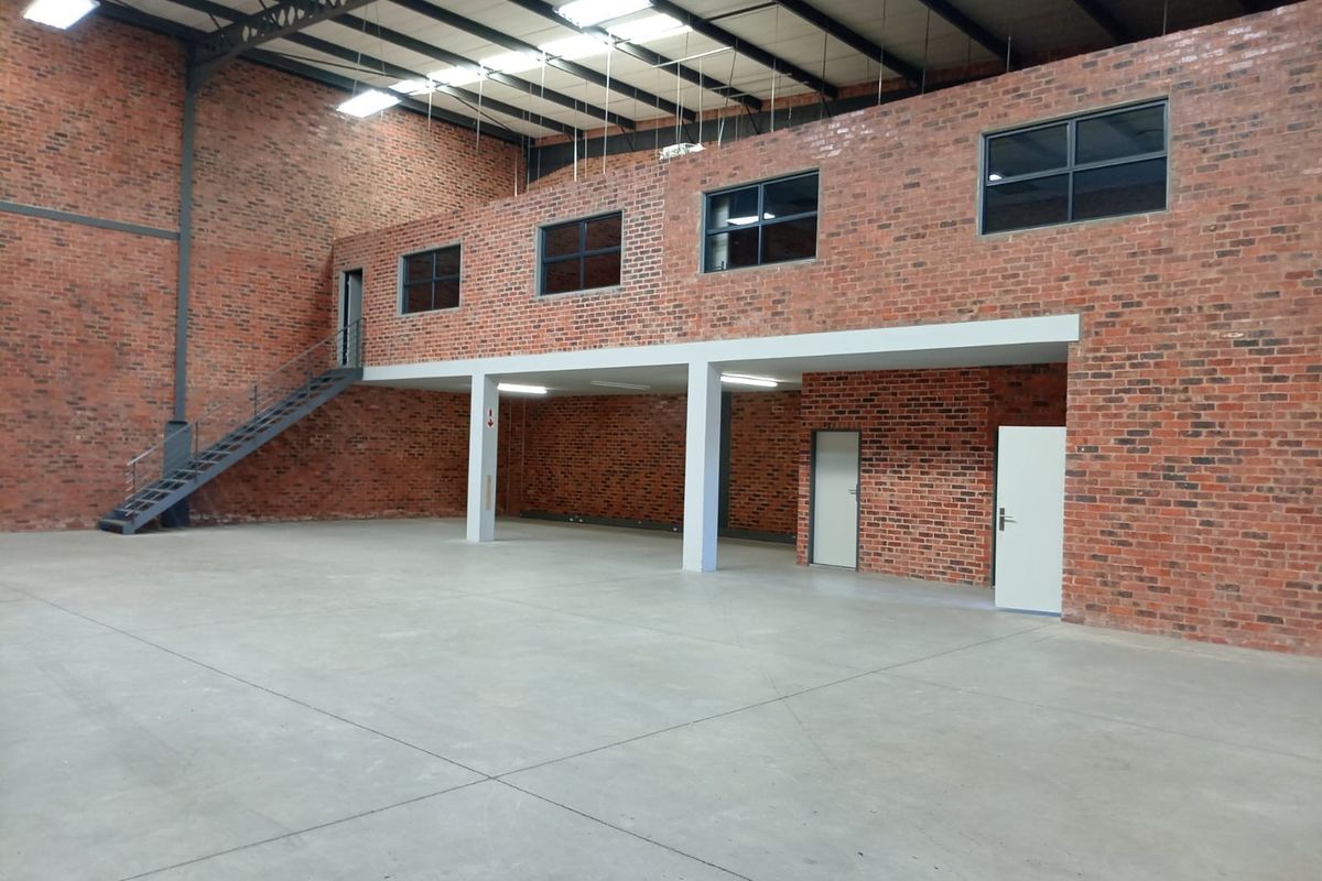 Spacious industrial warehouse unit featuring exposed brickwork, a mezzanine level with staircase, concrete flooring, and high-clearance ceilings with industrial lighting.