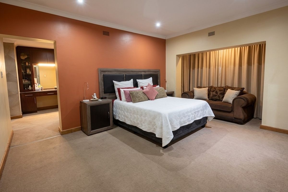 Spacious bedroom featuring neutral carpeting, a feature wall, recessed lighting, and an adjoining dressing area with built-in vanity cabinetry.