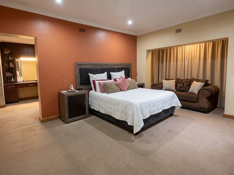 Spacious bedroom featuring neutral carpeting, a feature wall, recessed lighting, and an adjoining dressing area with built-in vanity cabinetry.