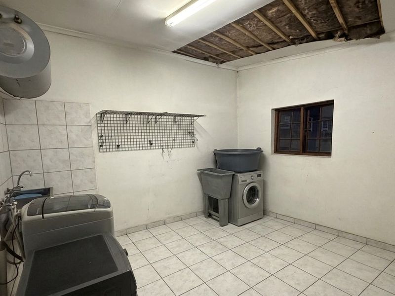 A functional laundry room featuring tiled flooring, a wall-mounted geyser, and a sink, currently requiring ceiling repairs and general cosmetic updates.