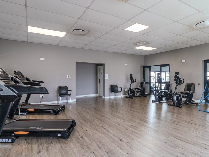 A spacious, well-lit gym facility featuring laminate flooring, suspended ceilings, and multiple exercise stations within a retirement village setting.