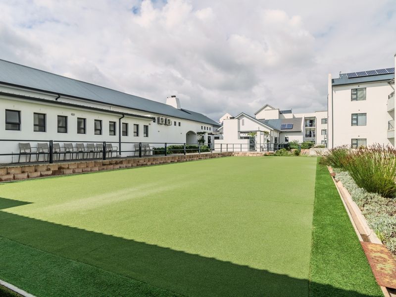 A well-maintained artificial turf bowling green located within the retirement village grounds, featuring perimeter fencing and surrounding landscaped garden beds.