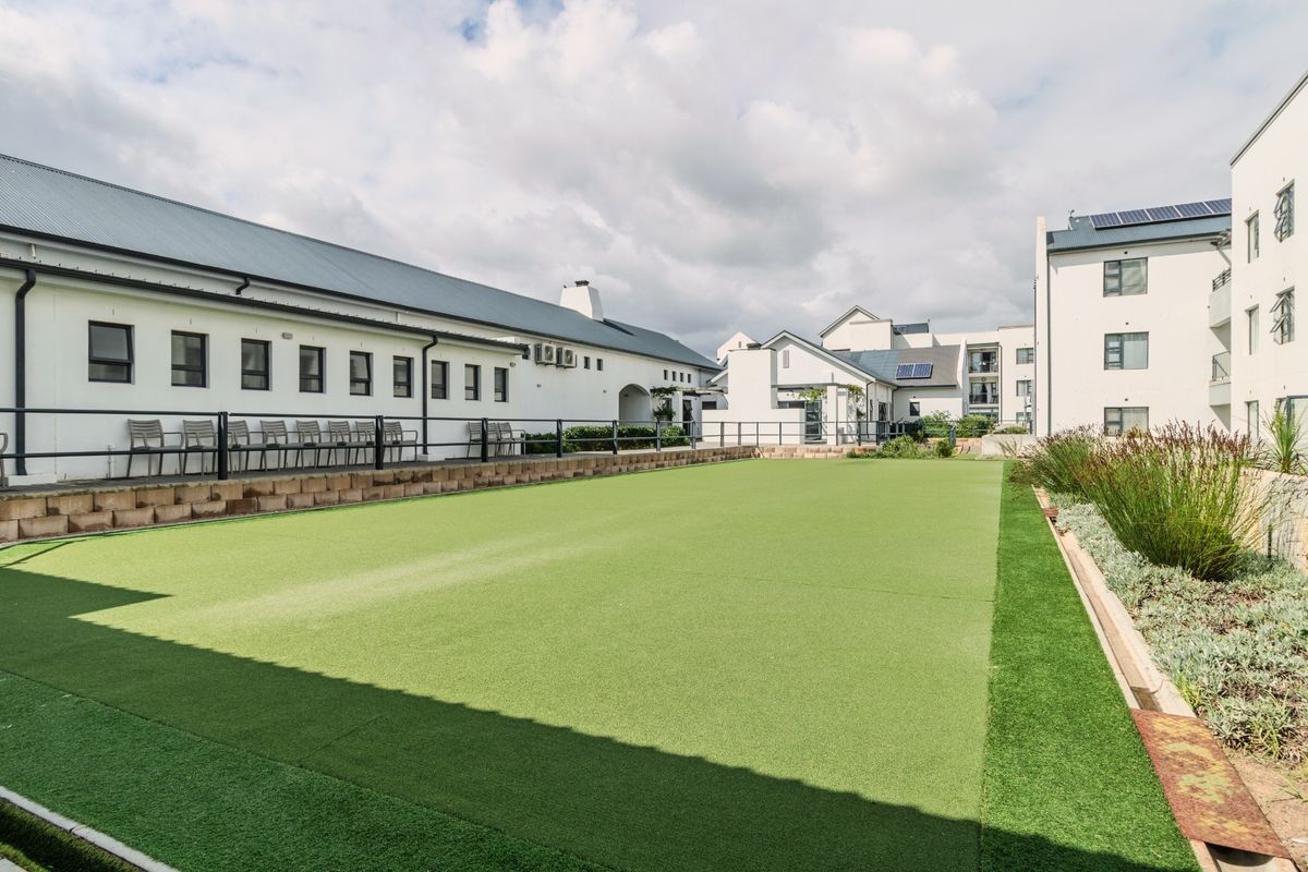 A well-maintained artificial turf bowling green located within the retirement village grounds, featuring perimeter fencing and surrounding landscaped garden beds.
