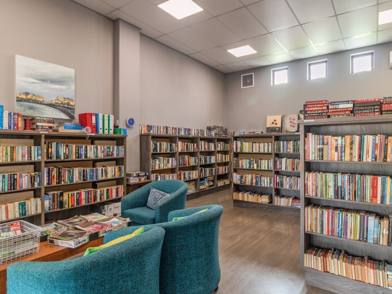 A well-maintained communal library space within the retirement village, featuring extensive built-in shelving, recessed lighting, and durable laminate flooring.