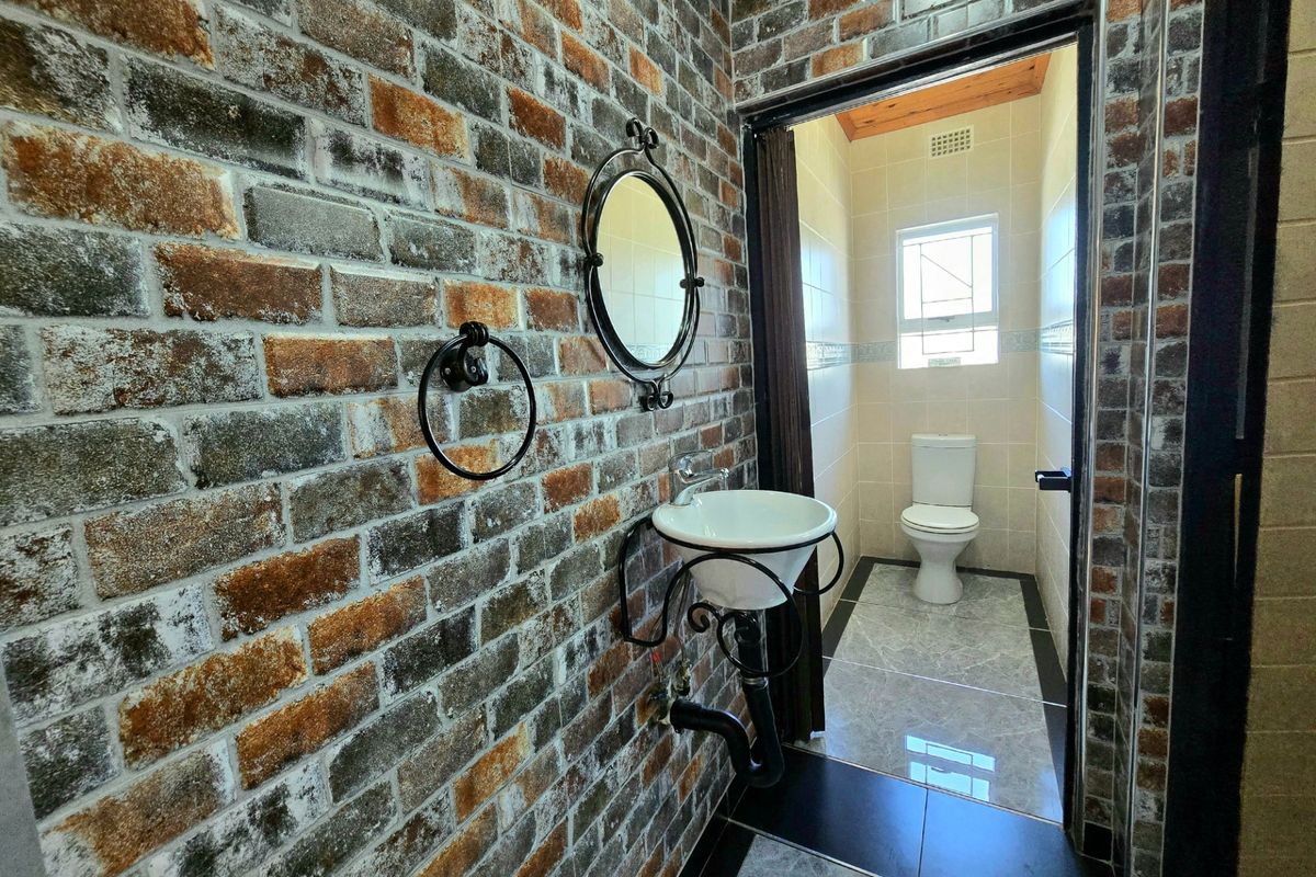 A bathroom featuring an exposed brick wall, a wall-mounted basin, and a separate toilet area with tiled flooring.
