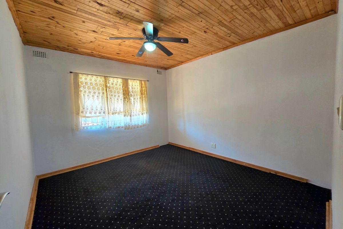 An empty bedroom featuring a timber-clad ceiling, a central ceiling fan, and dark patterned carpeting.