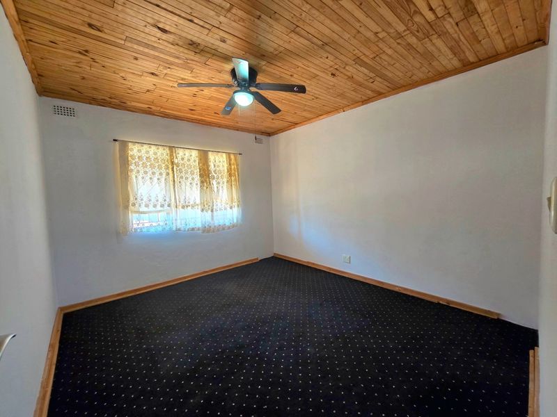 An empty bedroom featuring a timber-clad ceiling, a central ceiling fan, and dark patterned carpeting.