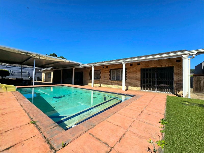 Outdoor pool area featuring a swimming pool, covered patio space, and brick exterior facade with security gates.