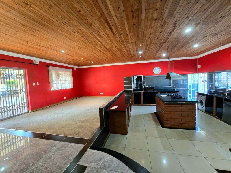 Spacious open-plan living and kitchen area featuring a timber ceiling, kitchen island with gas hob, and tiled flooring throughout the kitchen zone.