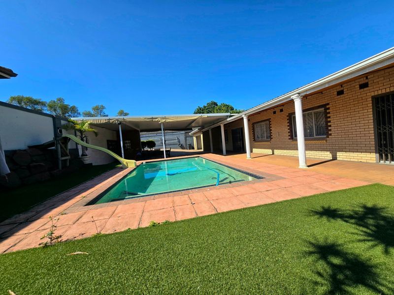 Outdoor pool area featuring a swimming pool with a slide, adjacent covered patio, and brick exterior wall with security-fitted windows.