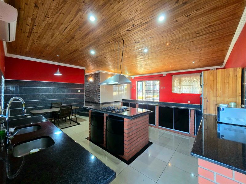 Spacious kitchen featuring a central island with gas hob, granite countertops, timber ceiling, and modern recessed lighting.