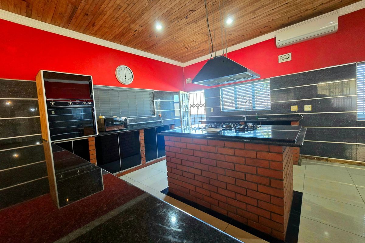 Spacious kitchen featuring granite countertops, a central brick island with a gas hob, built-in oven, and a distinctive timber ceiling.