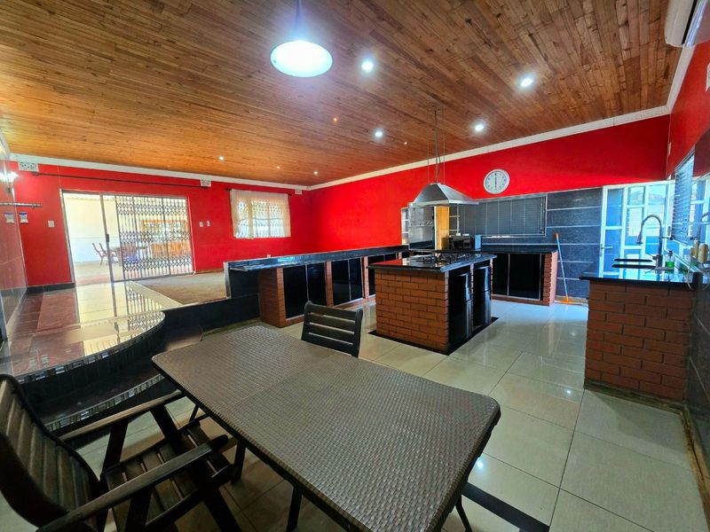 Spacious open-plan kitchen and living area featuring a central brick-based island, granite countertops, and a distinctive exposed timber ceiling.