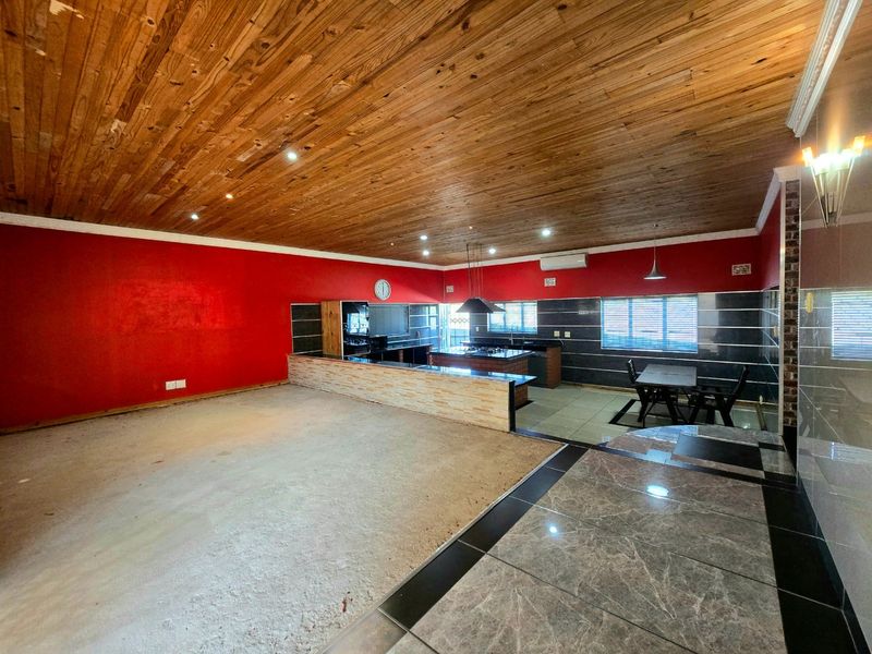 Spacious open-plan living and kitchen area featuring a timber ceiling, kitchen island with built-in appliances, and tiled flooring.