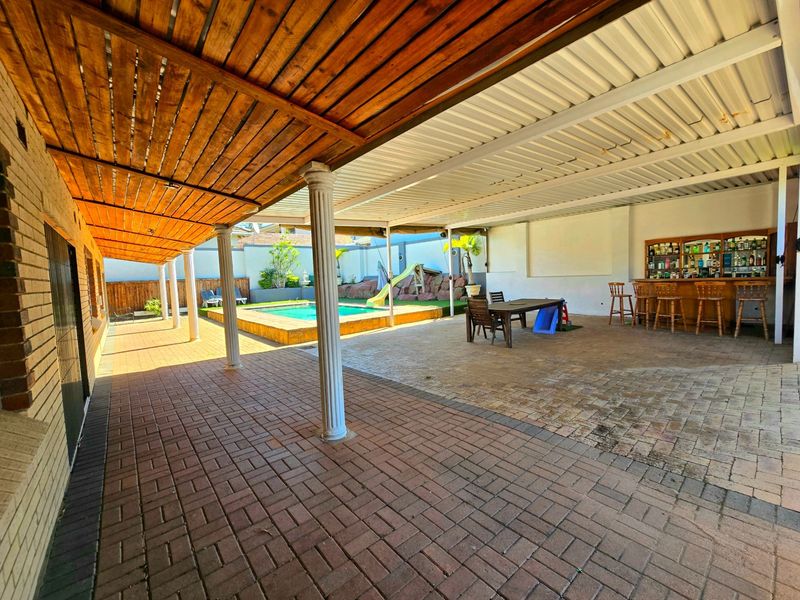 Spacious covered patio area featuring brick paving, a built-in bar, and direct access to an outdoor swimming pool.