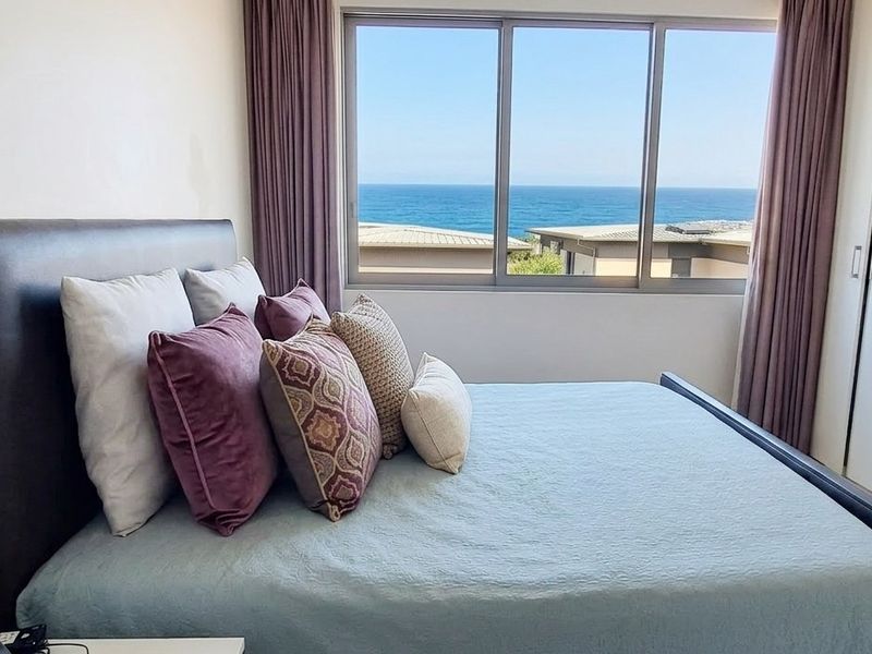 A bright bedroom featuring built-in cupboards and a large sliding window offering expansive ocean views.