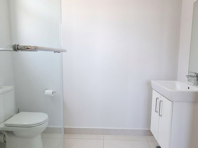 A clean, modern bathroom featuring a glass-enclosed shower, a white vanity with basin, and neutral floor tiling.