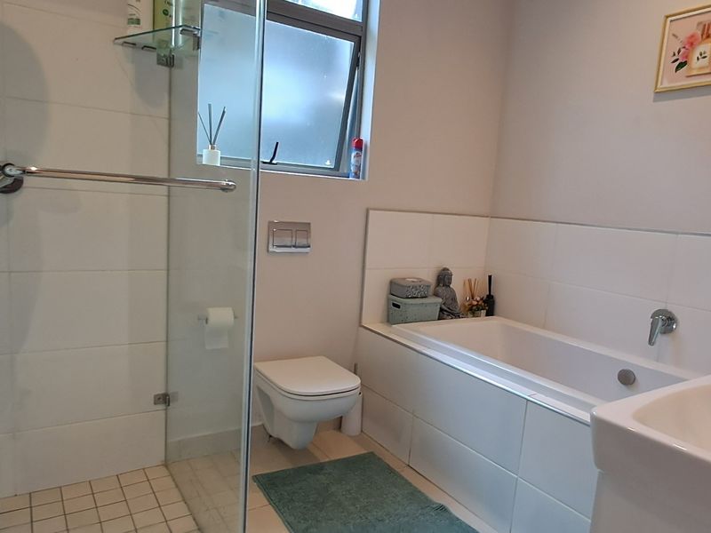 A modern, well-maintained bathroom featuring a glass-enclosed shower, a built-in bathtub, a wall-mounted toilet, and clean white tiling throughout.