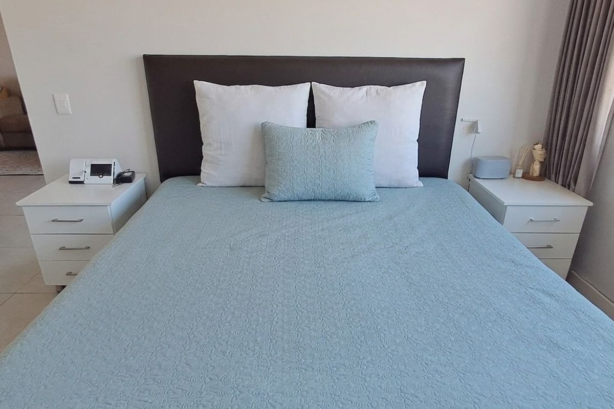 A well-maintained bedroom featuring neutral wall finishes, tiled flooring, and large windows with curtain tracks, offering a clean and functional living space.