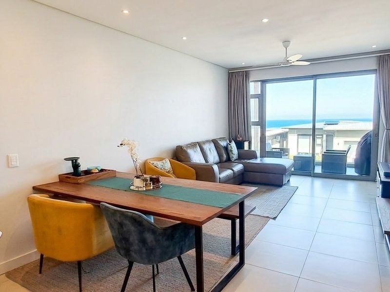 An open-plan living and dining area featuring tiled floors, recessed lighting, and large sliding glass doors that provide access to an outdoor balcony.