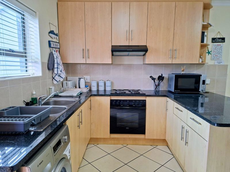 A functional kitchen featuring light wood cabinetry, granite countertops, a built-in oven with hob, and a stainless steel double sink.