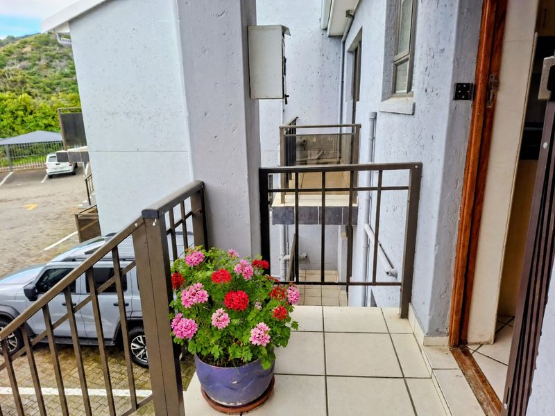 A functional balcony area featuring tiled flooring and metal safety railings, overlooking the apartment complex parking area.