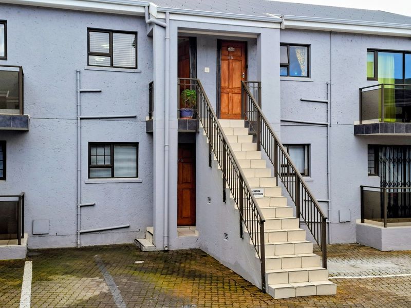 Exterior view of an apartment building featuring a central staircase leading to upper-level entrances, paved driveway, and aluminium window frames.