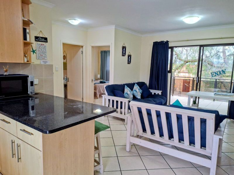 Open-plan living area featuring a kitchen with granite countertops and tiled flooring, leading directly to a balcony through sliding glass doors.