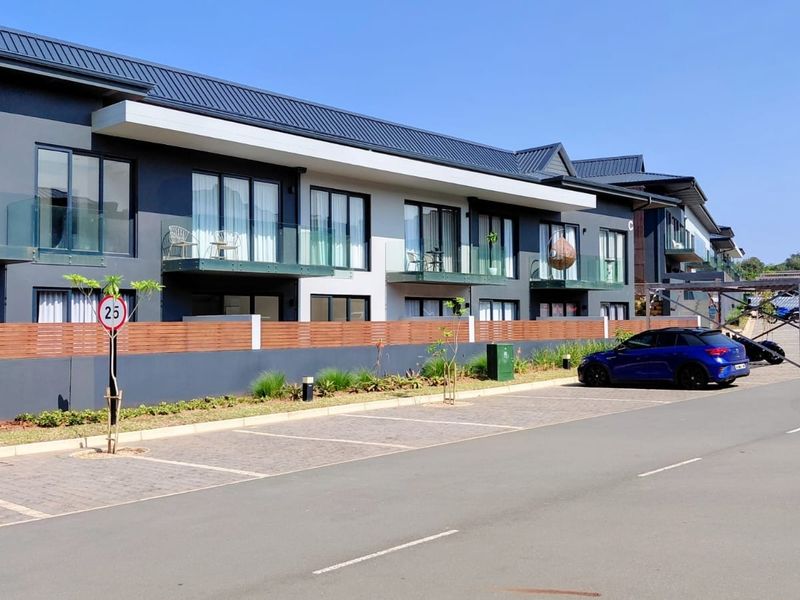 Modern multi-story residential complex featuring contemporary architecture, glass balcony balustrades, paved parking bays, and secure timber fencing.