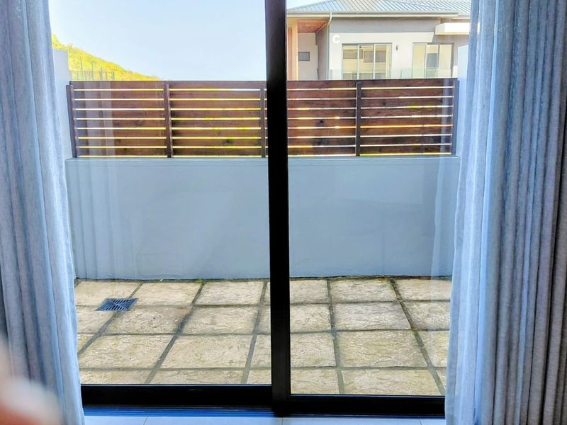A private paved patio area featuring a timber slat privacy screen, accessible through a sliding glass door.