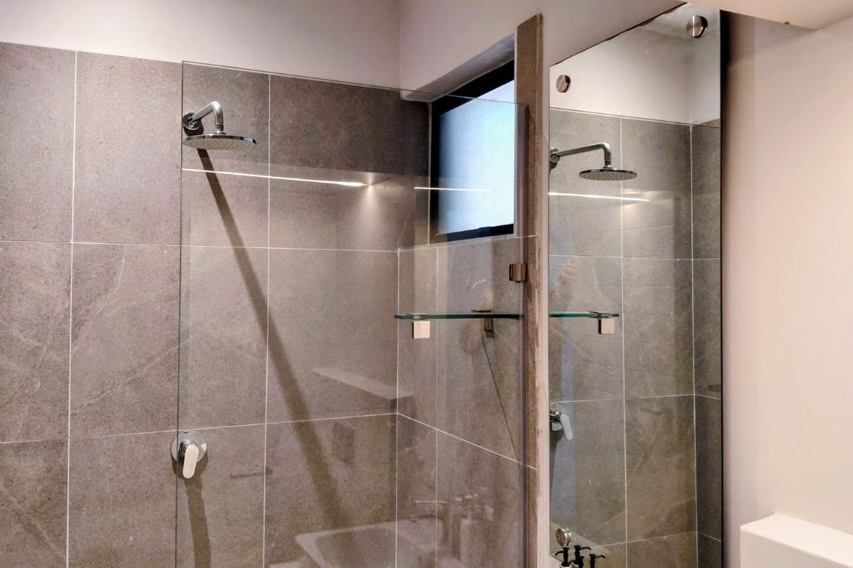 A modern, well-maintained walk-in shower featuring large-format grey tiles, a glass screen, and a contemporary rain shower head.