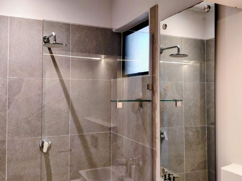 A modern, well-maintained walk-in shower featuring large-format grey tiles, a glass screen, and a contemporary rain shower head.