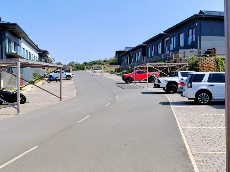 A view of the residential complex street featuring paved parking bays, covered carport structures, and modern multi-story building facades.