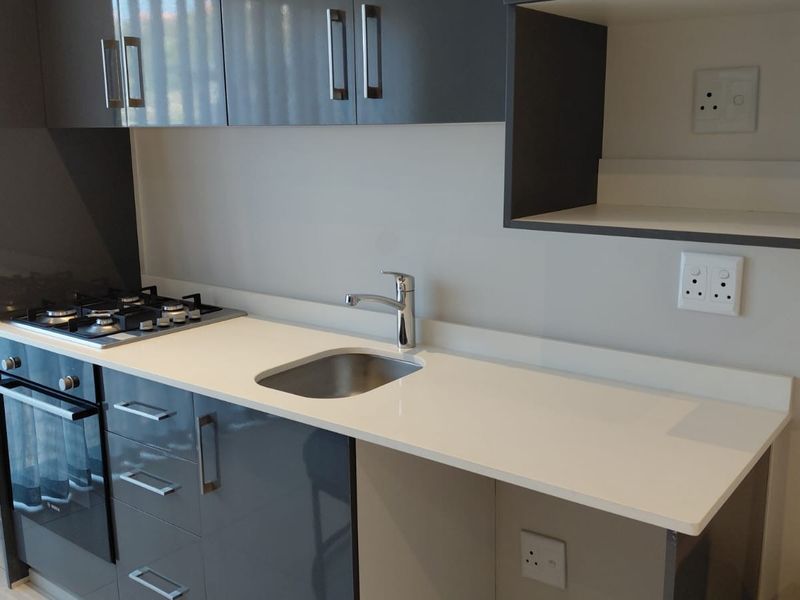 Modern kitchen featuring sleek grey gloss cabinetry, white quartz countertops, a built-in gas hob, oven, and a stainless steel sink.