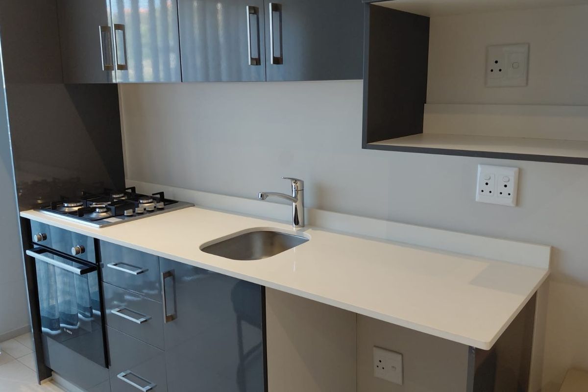 Modern kitchen featuring sleek grey gloss cabinetry, white quartz countertops, a built-in gas hob, oven, and a stainless steel sink.