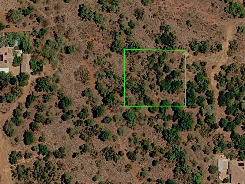 An aerial view of a vacant residential plot featuring natural vegetation and surrounding landscape.
