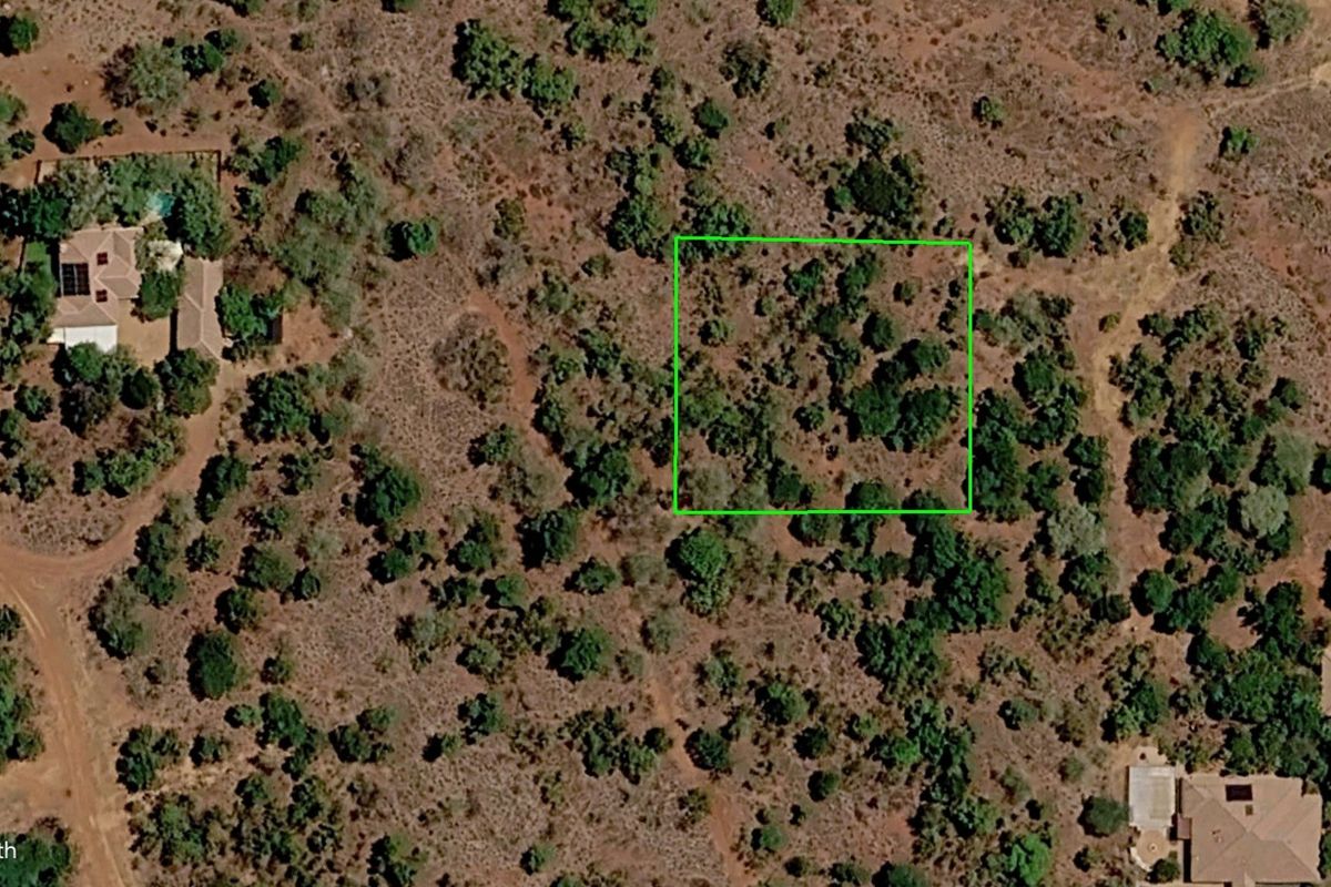 An aerial view of a vacant residential plot featuring natural vegetation and surrounding landscape.