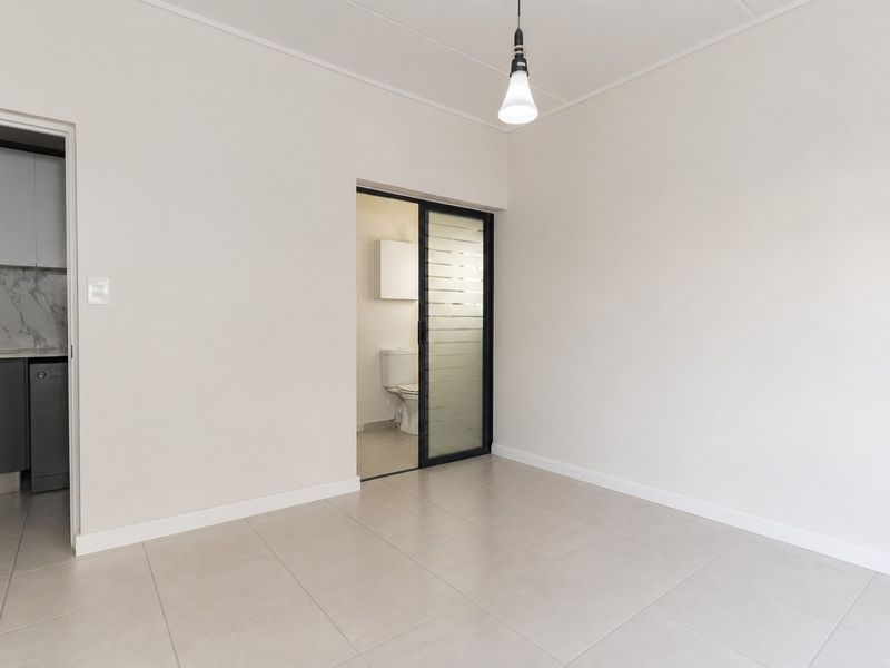 A bright, empty living area featuring neutral tiled flooring, a modern sliding glass door, and a simple pendant light fixture.
