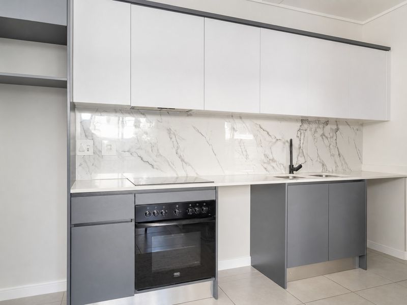 Modern kitchen featuring sleek grey and white cabinetry, marble-look splashback, built-in oven, electric hob, and stone countertops in a clean, contemporary finish.