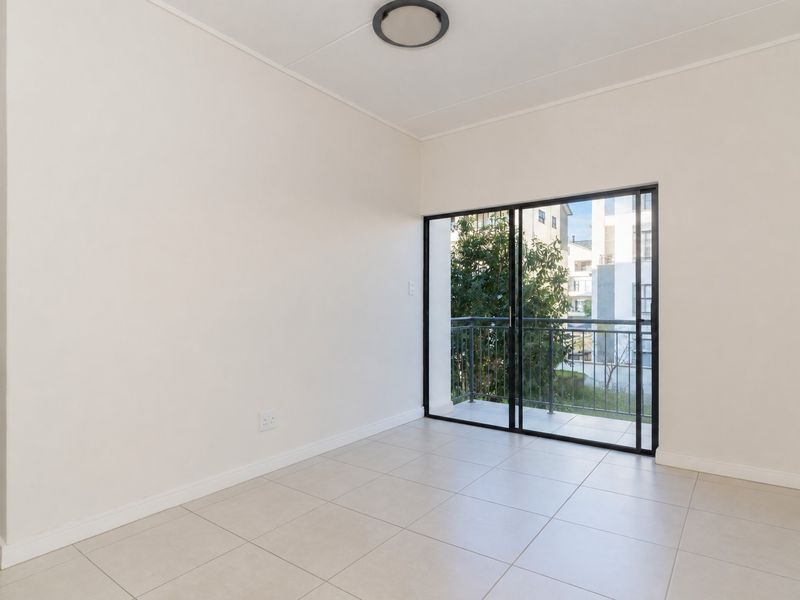 A bright, empty bedroom featuring neutral tiled flooring, a modern ceiling light, and a sliding glass door providing access to a private balcony.