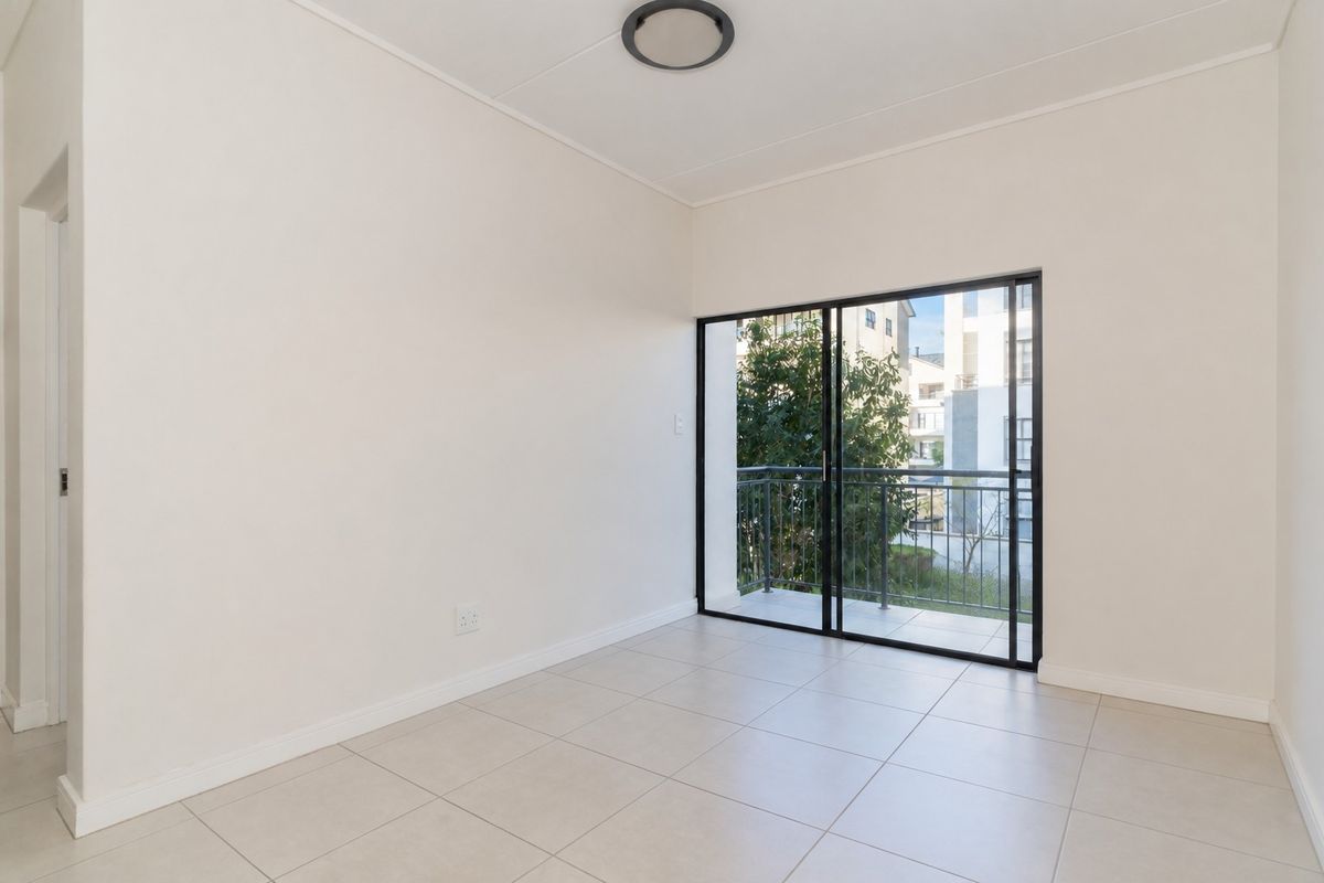 A bright, empty bedroom featuring neutral tiled flooring, a modern ceiling light, and a sliding glass door providing access to a private balcony.