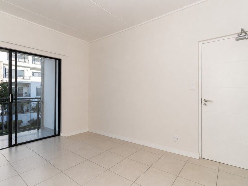 A bright, empty bedroom featuring neutral tiled flooring, a sliding glass door leading to a balcony, and a modern interior door with a closer.